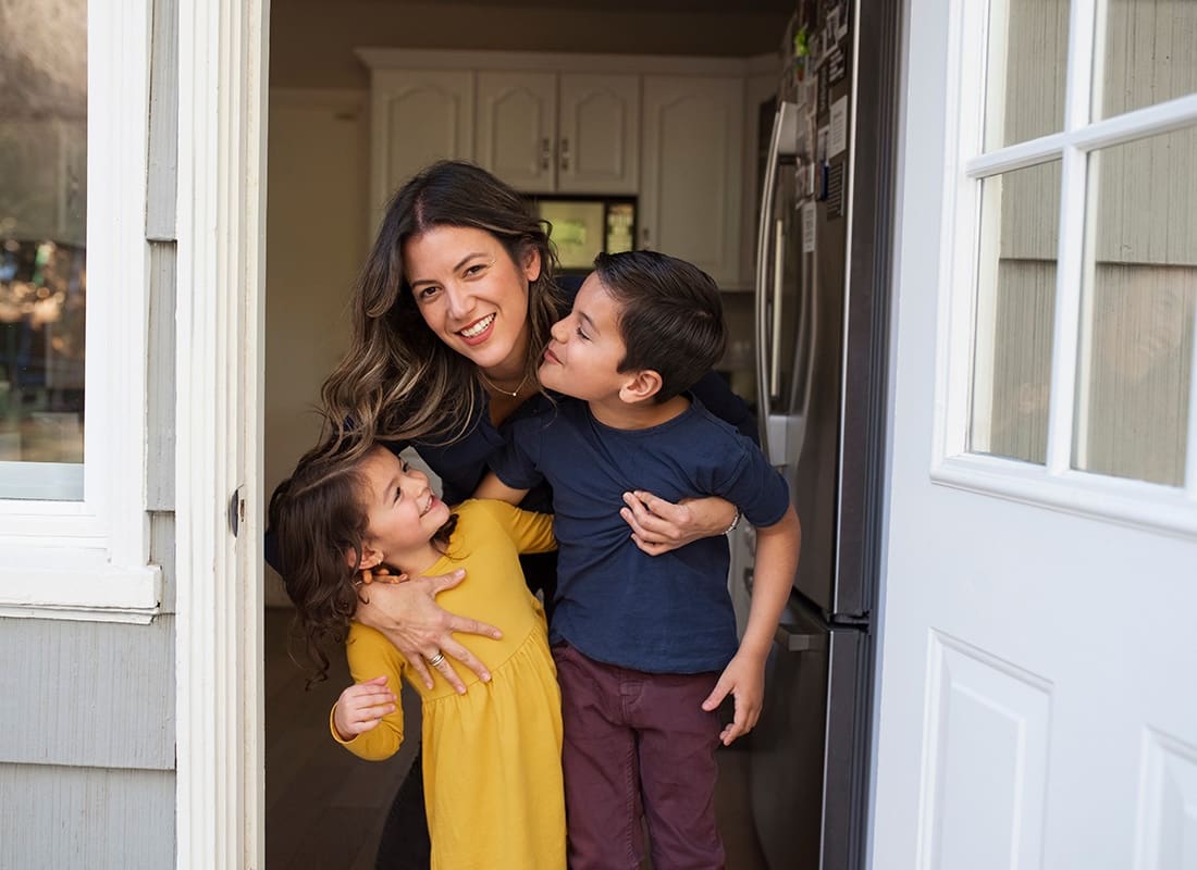 We Are Independent - Portrait of a Cheerful Young Mom Hugging her Son and Daughter Whie Standing in the Front Doorway of their Home